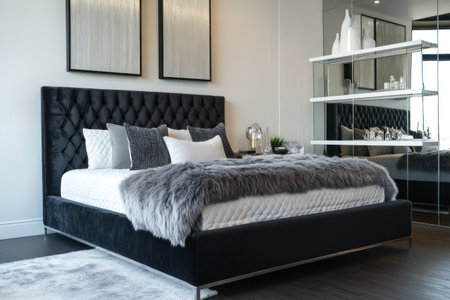 A small bedroom with a large bed, a black fabric headboard, and a silver metal frame. On the right side of the room, there are white glass shelves. In the foreground, there is a gray fluffy blanket. Above the bed, there are two large square mirrors. The floor is made of dark wood, and the interior design is in a modern style. The walls are white, with a gray accent wall. The camera used is a Sony Alpha A7 III. --ar 3:2 --v 6.1 Job ID: dcd8003e-0912-4a8d-b278-fafeefdde417の素材