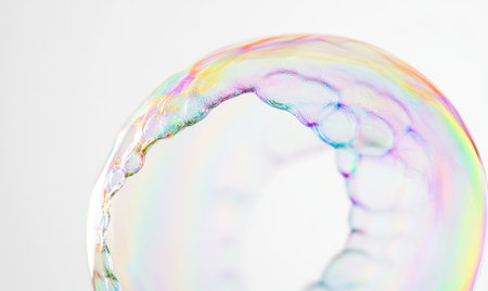 A close-up of the edge of an iridescent soap bubble, with rainbow colors and blurred edges against a stark white background. The focus is on capturing the delicate balance between light refraction on the bubble's surface, creating intricate patterns that reflect across its transparent exterior. This image symbolizes minimalism and simplicity, emphasizing vibrant coloration and the dynamic interplay of light within the form of the soap bubble. --ar 5:3 --v 6.1 Job ID: b9a21141-c617-40e1-995d-615bcc0458b8の素材