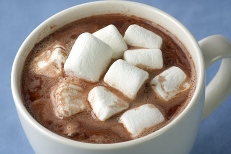 A mug of hot chocolate topped with fluffy white marshmallows, close-up against a blue backdropの素材