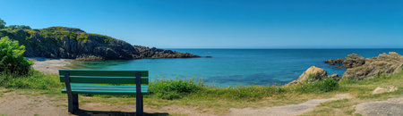 Panoramic view of the coast and cliffs at Guernsey on a clear day, with an empty green bench overlooking calm turquoise waters and lush coastal vegetation under a clear blue sky. The picturesque scene captures the vibrant colors of nature against a backdrop of rugged coastline. This photograph highlights the beauty and tranquility found on the Channel Islands. --ar 52:15 --v 6.1 Job ID: 8128aa21-d883-4b50-83be-e7bc1755b1b6の素材