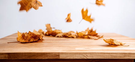 The image captures falling autumn leaves on a wooden surface, set against a plain white backdrop. The leaves display warm hues of brown and yellow, suggesting a fall season. This composition could be used for various commercial purposes, suitable for product presentations or seasonal promotions.の素材