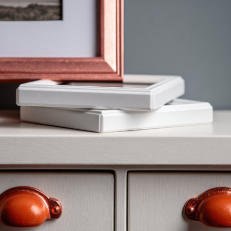 This image showcases a stack of white picture frames atop a table, complemented by an attached copper-colored frame. The composition emphasizes clean lines and a neutral color palette. The lighting appears soft, indicating an indoor setting. It may be suitable for visual elements in design or for marketing materials.の素材