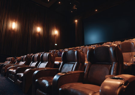 Rows of luxurious seating fill a darkened cinema, illuminated by subtle lighting. The image showcases the plush, brown leather seats and the empty screen awaiting a presentation. The composition creates a sense of anticipation and is suitable for commercial and editorial applications, possibly related to entertainment or media.の素材