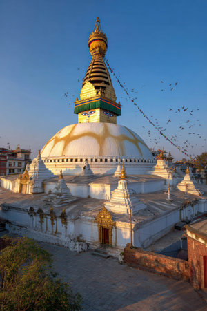 An overhead view reveals a large stupa, displaying intricate architecture and cultural significance. The structure features white and gold tones, contrasting against a clear, blue sky, enhanced by sunlight. The scene suggests a historic or religious site, suitable for commercial or editorial applications related to travel or cultural themes.の素材