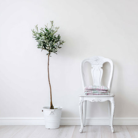 A minimalist interior setting showcases a potted olive tree beside a white ornate chair against a clean white backdrop. The composition is characterized by high-key lighting, emphasizing the textures and forms within the scene. Suitable for a range of commercial applications, the image evokes a sense of tranquility and elegant simplicity.の素材