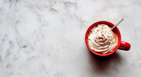 An overhead view displays a red mug filled with a beverage and topped with whipped cream and a dusting. The scene is illuminated by natural light, resting on a white and gray marble surface. The image could be suitable for use in food blogs, advertising, or related editorial content.の素材