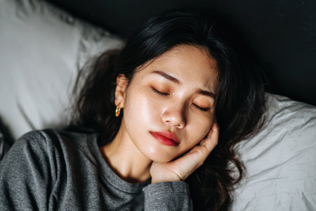 A woman rests on a pillow, eyes closed, hand on cheek, appearing peaceful and asleepの素材