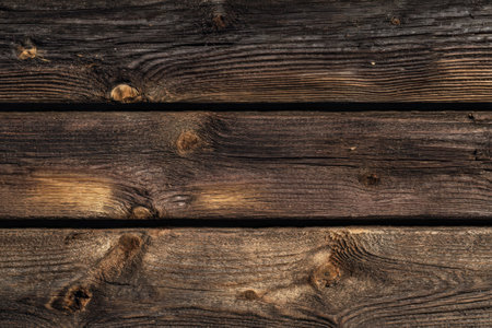 Close-up of weathered wooden planks, showing grain and knots, in varying shades of brownの素材