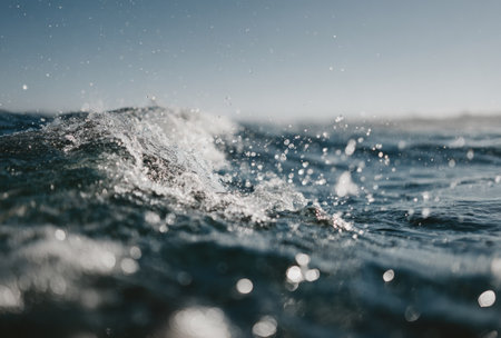A close-up shot of a cresting wave in the ocean with sunlight scattering dropletsの素材