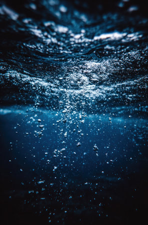 Underwater shot captures upward rising bubbles, illuminated by filtered light, in deep blue waterの素材