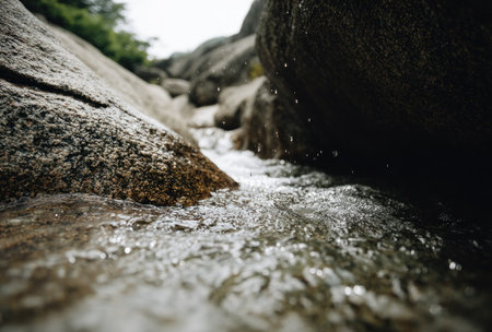 Close-up shot of water flowing between large, textured rocks in a natural streamの素材