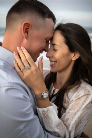 couple, beach and love with hands on face while holding engagement ring of commitment together, created with generative aiの素材
