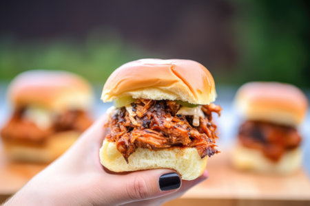 hand holding finishing spicy bbq pork slider against grill backdrop, created with generative aiの素材