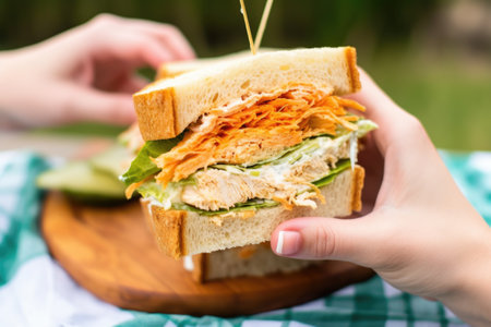 hand lifting a buffalo chicken sandwich from a picnic basket, created with generative aiの素材