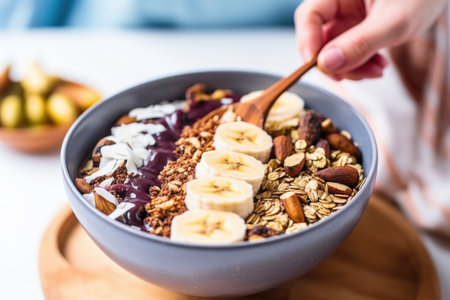 hand using a spoon to scoop acai bowl loaded with granola and banana slices, created with generative aiの素材