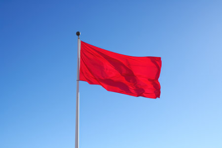 red flag fluttering against a clear blue sky, created with generative aiの素材