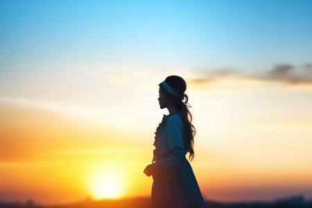 silhouette of a woman greeting the sunrise on a hilltopの素材