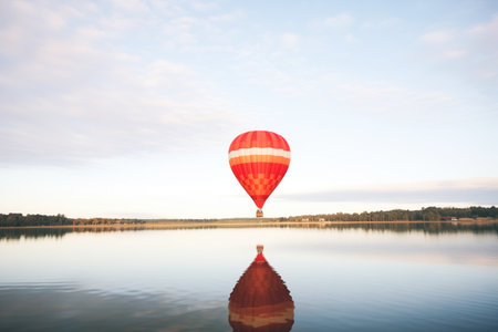 solo red hot air balloon floating above a calm lakeの素材