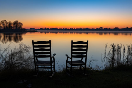 empty twin chairs facing calm lake during sunriseの素材