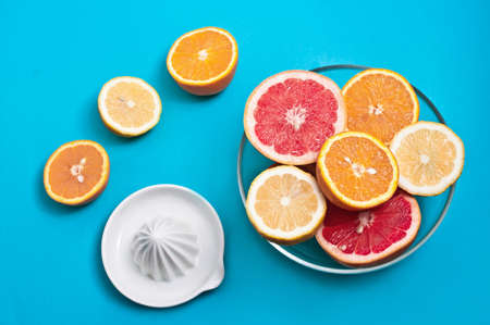 Oranges lemons and pink grapefruits in a bowl and a squeezer on a blue background