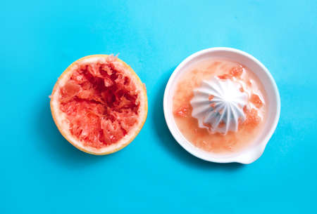 Juiced Red Grapefruit with a squeezer on blue backgroundの写真素材
