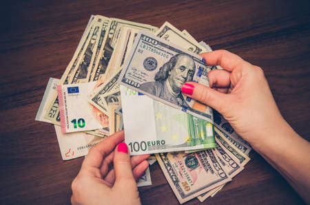 woman holding euro and dollar banknotes over wooden table