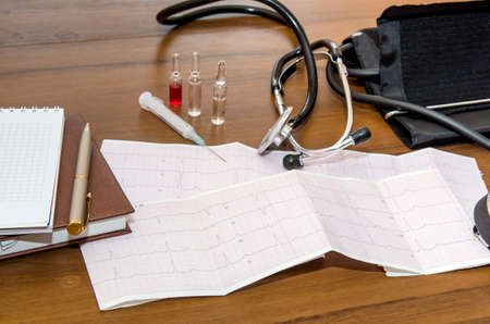 Medicine concept. Cardiogram, syringe, stethoscope, notepad on table