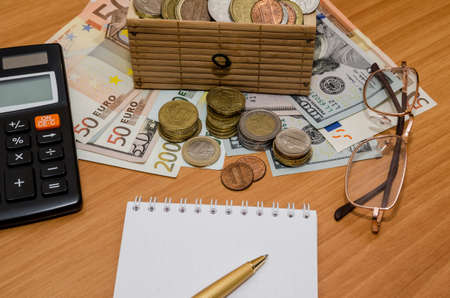 open treasure chest with coin. Us dollar and euro with empty notepad, glasses and calculatorの写真素材