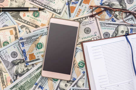 dollar as background, phone, pen and notebookの写真素材