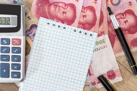 100 yuan with calculator and notepad, pen on desk.の写真素材