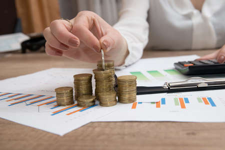 Savings, female hand stacking euro coins into columns above business diagram