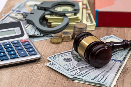 Law gavel with handcuffs, dollars and books as background, close up.の写真素材