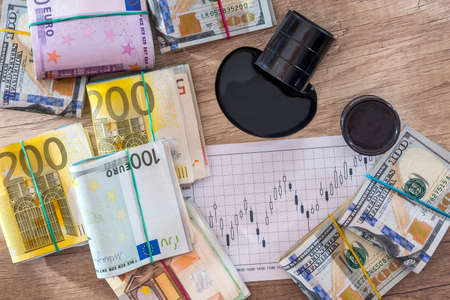 dollars and euro banknote with spilled oil on desk. calculator with oil production schedule. business concept.の写真素材