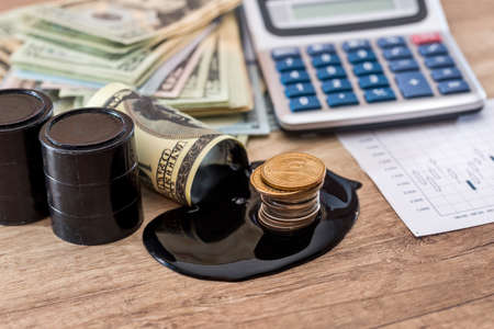 dollars banknote with spilled oil on desk. calculator with oil production schedule. business concept.の写真素材