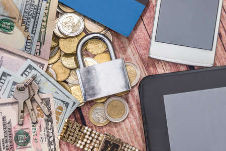 lock, dollar banknote, coin, tablet and phone on desk.の写真素材