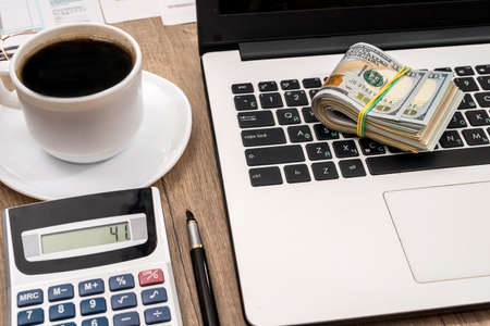 stack of dollar, cup of coffee and laptop on deskの写真素材