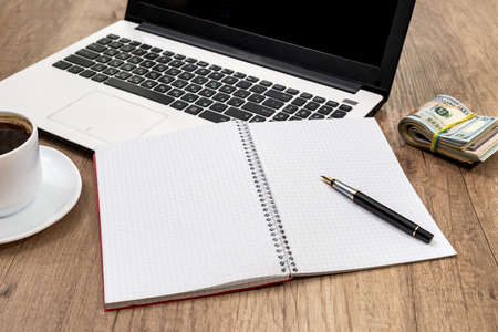 business concept - laptop with notepad, cup of coffee and dollar