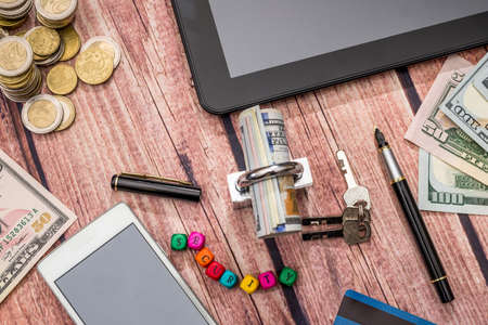 lock, dollar banknote, coin, tablet and phone on desk.