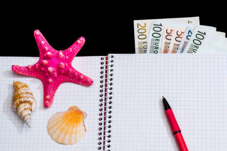 Blank open notepad with seashells, pen and dollar isolated on black backgroundの写真素材