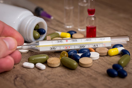 different pills and thermometer on wooden background