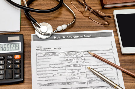 health insurance claim form with stethoscope on clipboard, syringe, calculator and penの写真素材