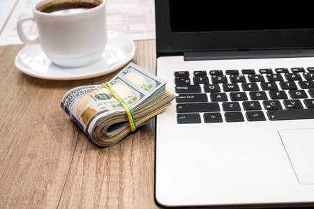 stack of dollar, cup of coffee and laptop on deskの写真素材