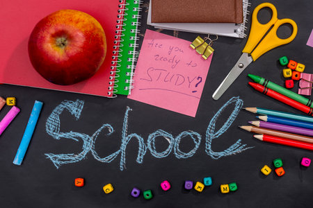 many school supplies and apples on black blackboard