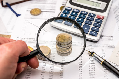 magnifying glass with financial documents, coin, notepad, calculator and penの写真素材