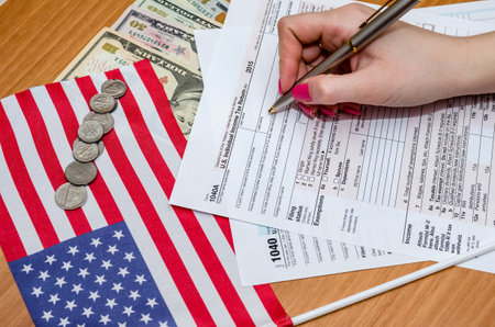 Business woman fills the tax form 1040 with money, pen, flag of USA and calculatorの写真素材
