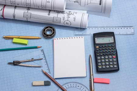 blank notepad, rolls of engineering drawings with tools on graph backgroundの写真素材