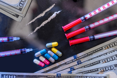 syringe with heroine, pills, us money isolated on black glass.