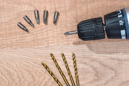 Drill and set of golden drill bits on wooden background