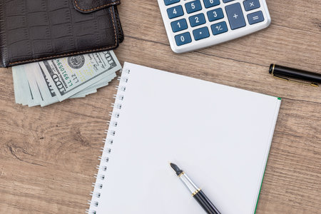 notepad with pen, calculator, dollar bills on desk.