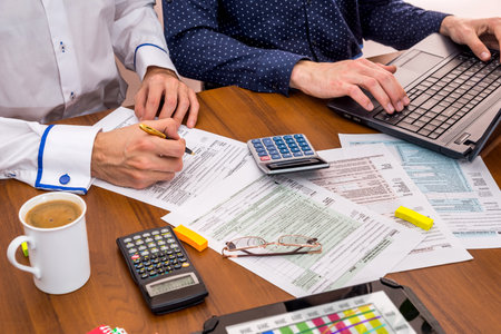 two people filling tax forms, helping each other.
